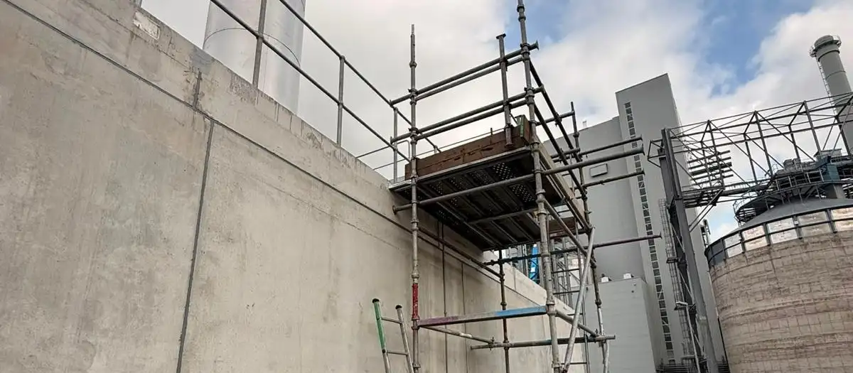 Scaffold tower with a ladder gate and scaffold tag against a concrete wall on an industrial site