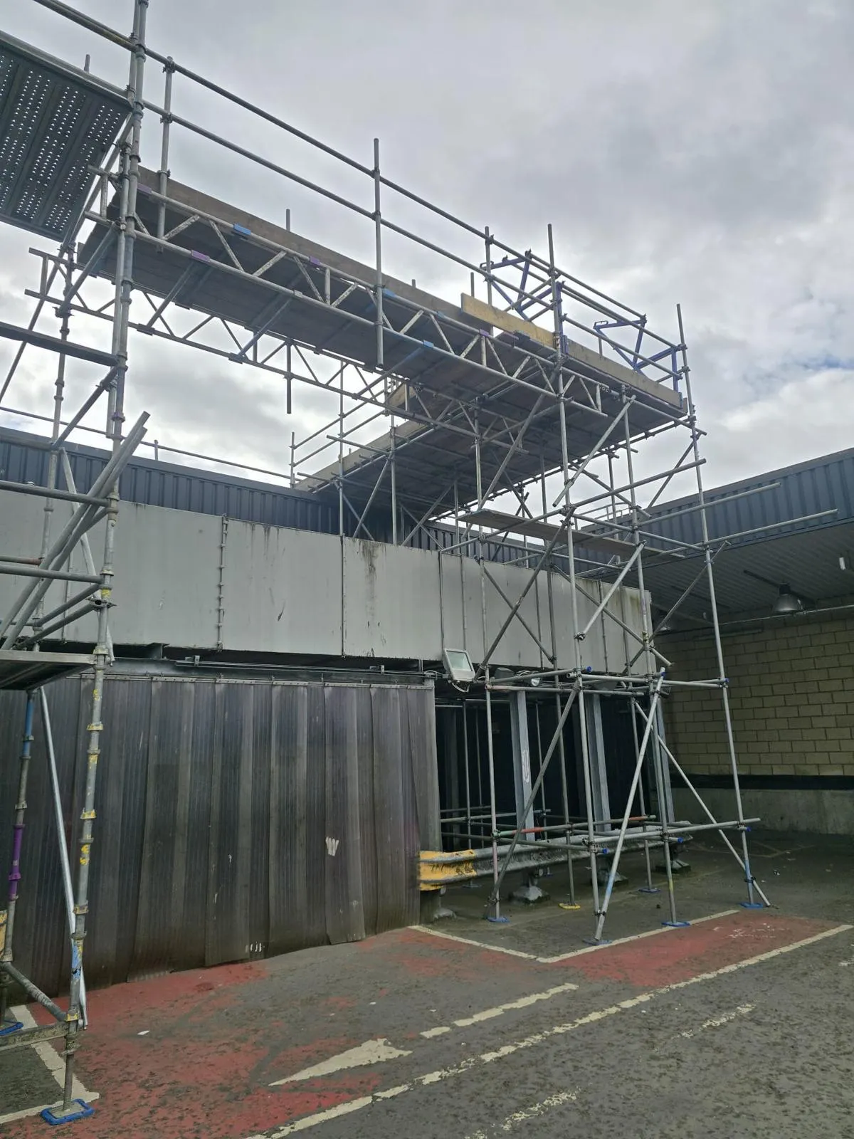 Scaffold rising over a single-storey bay to a beamed platform on an industrial building