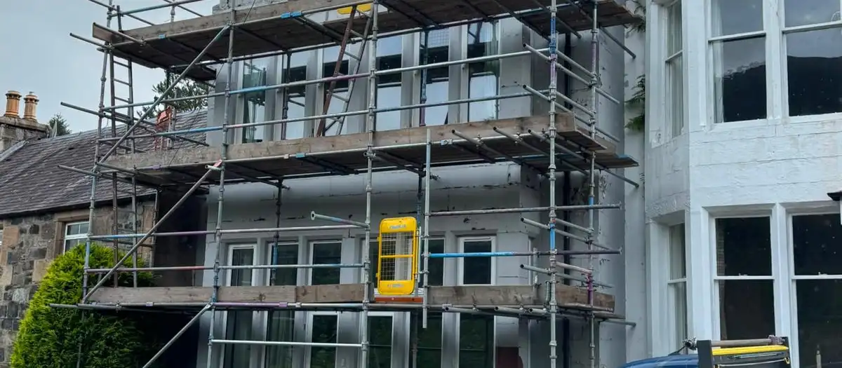 Scaffolding on the front of a white-painted house, with an M.F Scaffold banner and van