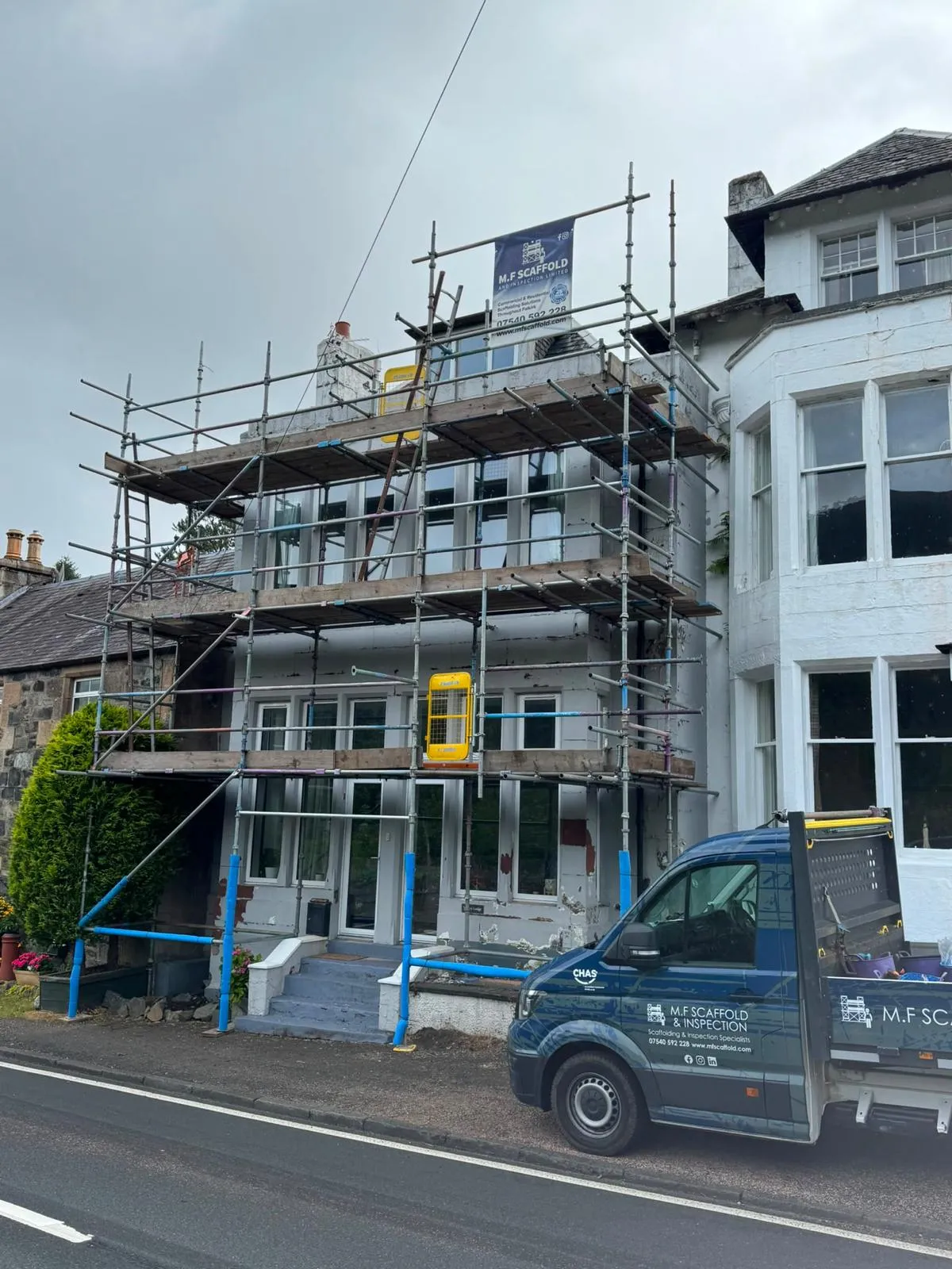 Scaffolding on the front of a white-painted house, with an M.F Scaffold banner and van