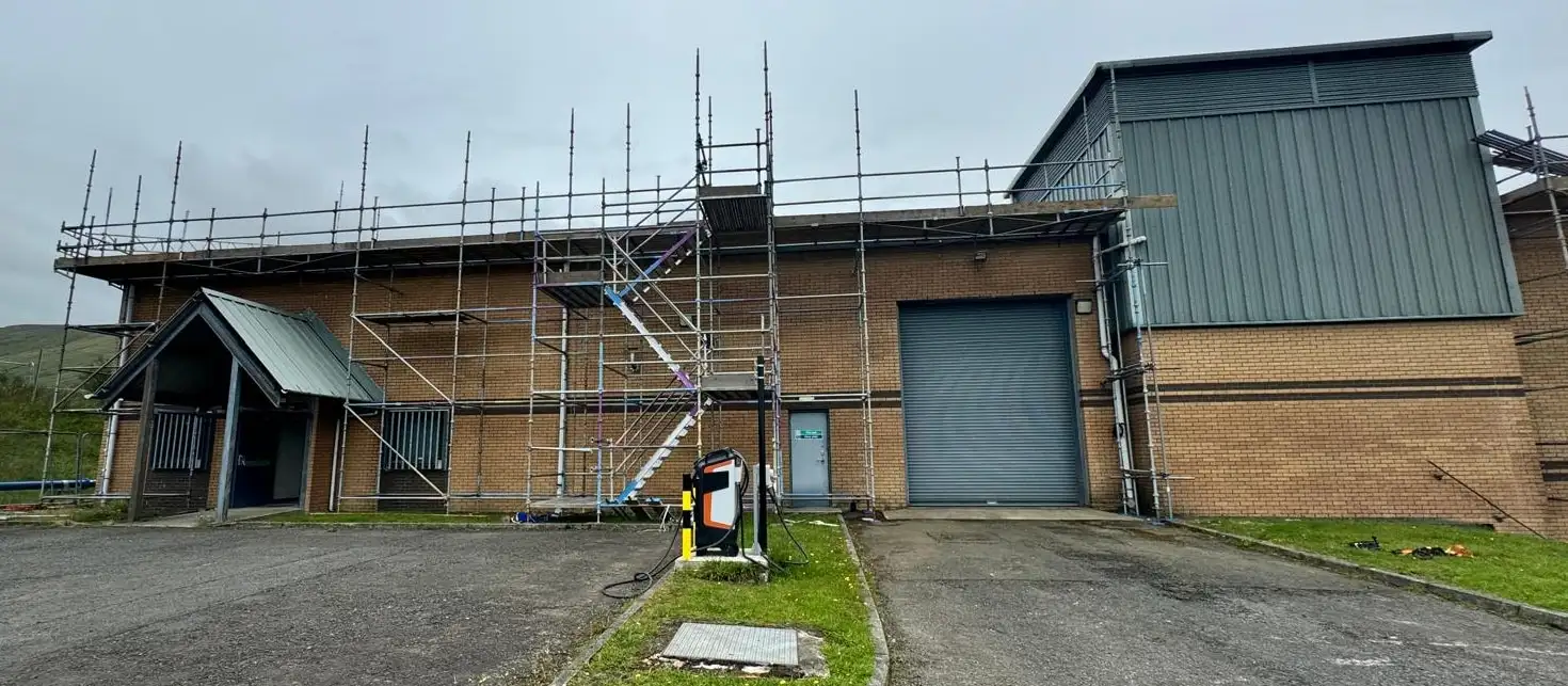 Eaves-level scaffolding with a stair tower along a brick industrial unit