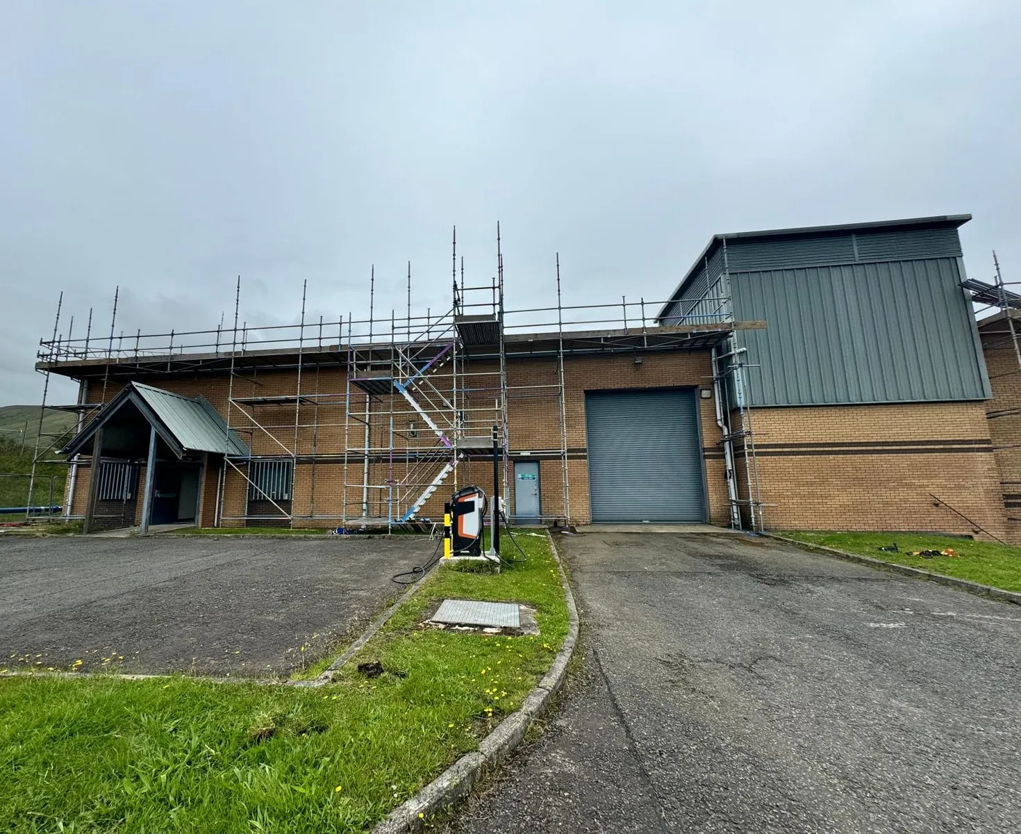 Eaves-level scaffolding with a stair tower along a brick industrial unit