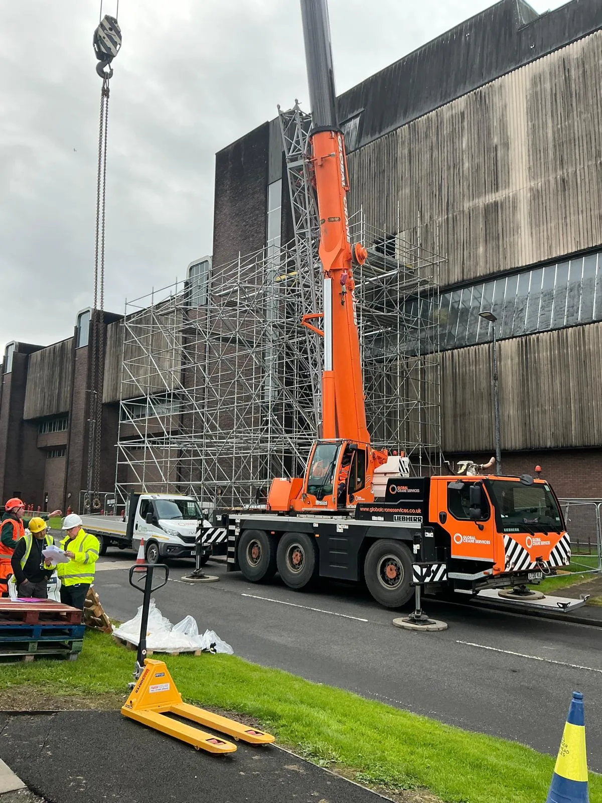 Site team checking drawings beside a mobile crane, with a large scaffold on the building behind