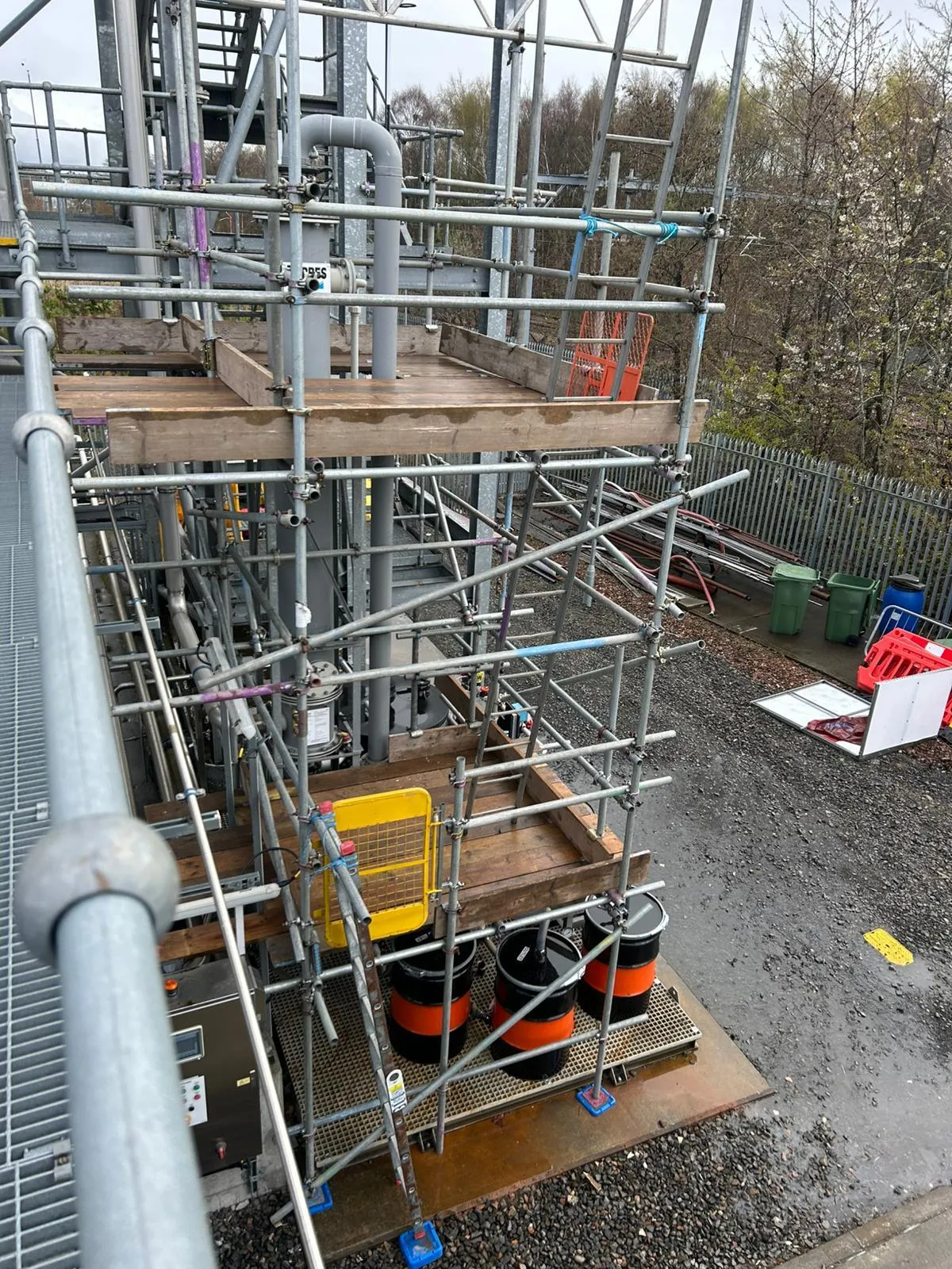 Scaffold tower with boarded platforms and a ladder gate around pipework, seen from above