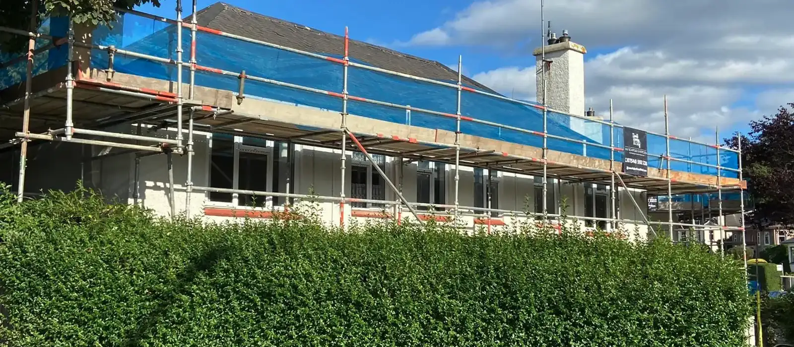 Scaffolding along the front of a home with the roof sheeted in blue