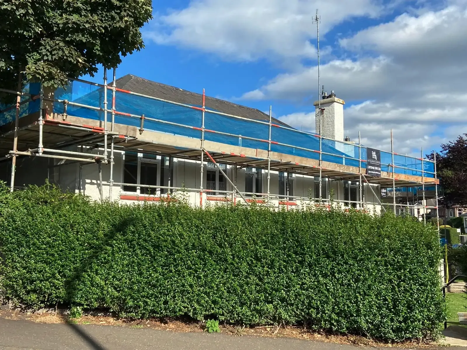 Scaffolding along the front of a home with the roof sheeted in blue