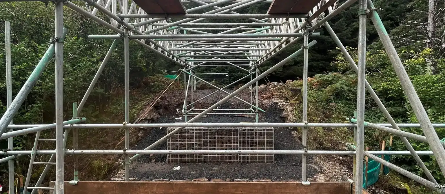 Access bridge with a boarded deck and handrails spanning between stone walls