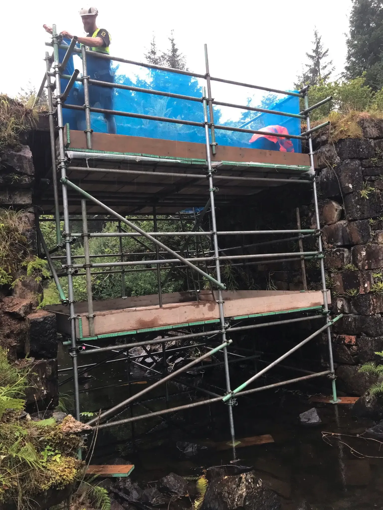 Scaffold tower built against a stone wall, sheeted at the top