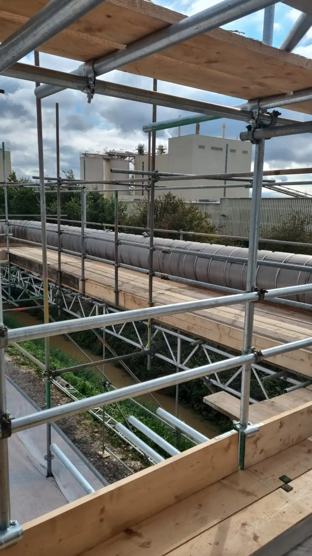 Boarded scaffold running alongside a long pipe run on an industrial site