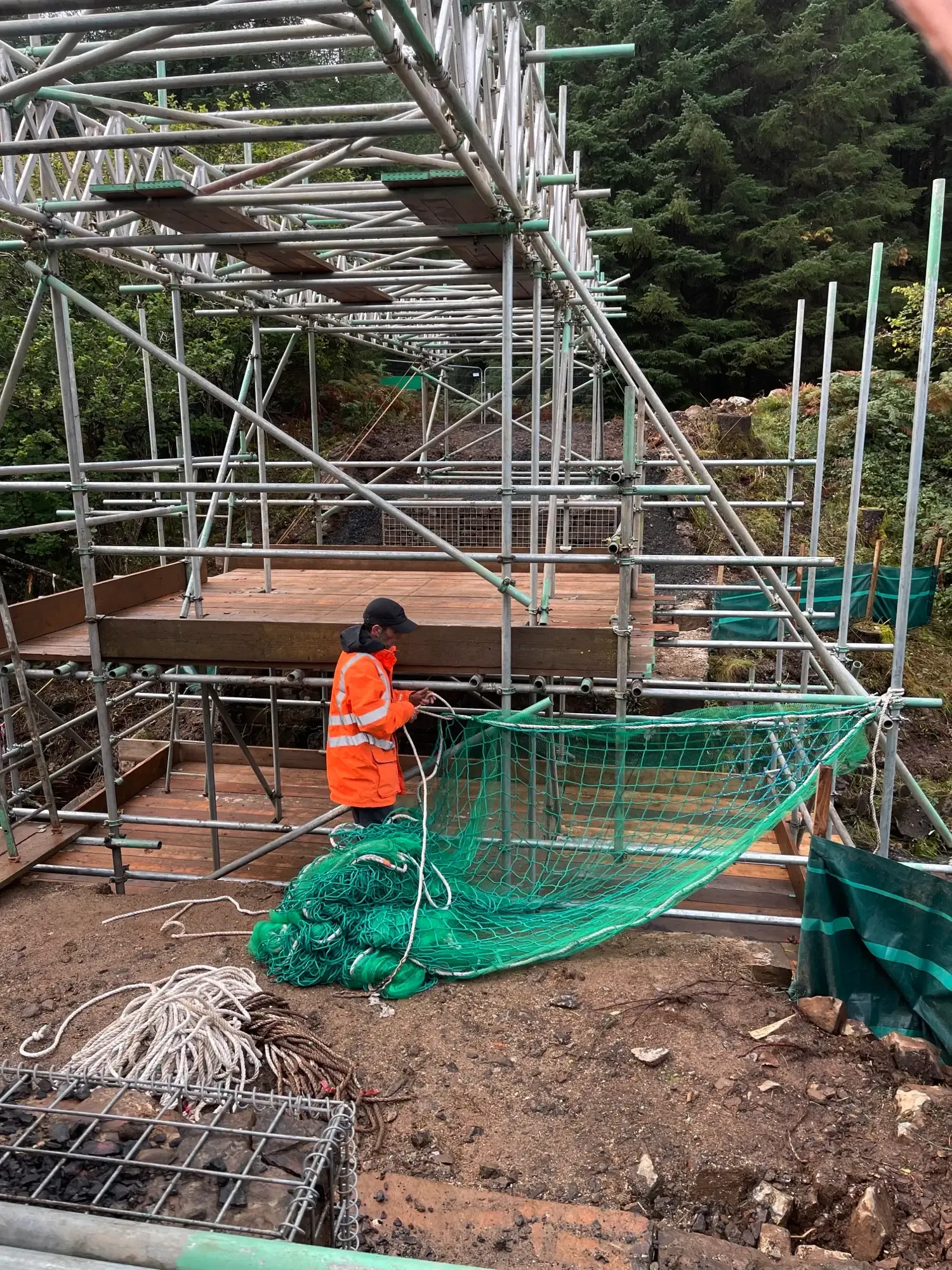 Scaffolder in hi-vis fitting netting to a large scaffold structure under construction