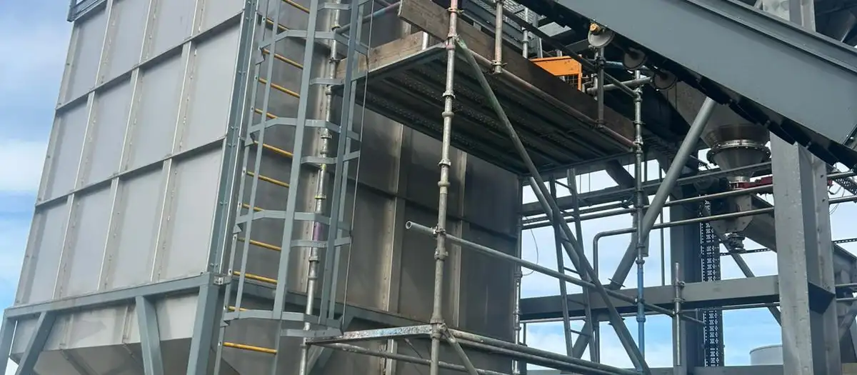 Scaffold tower built around a hopper and conveyor beneath steel silos