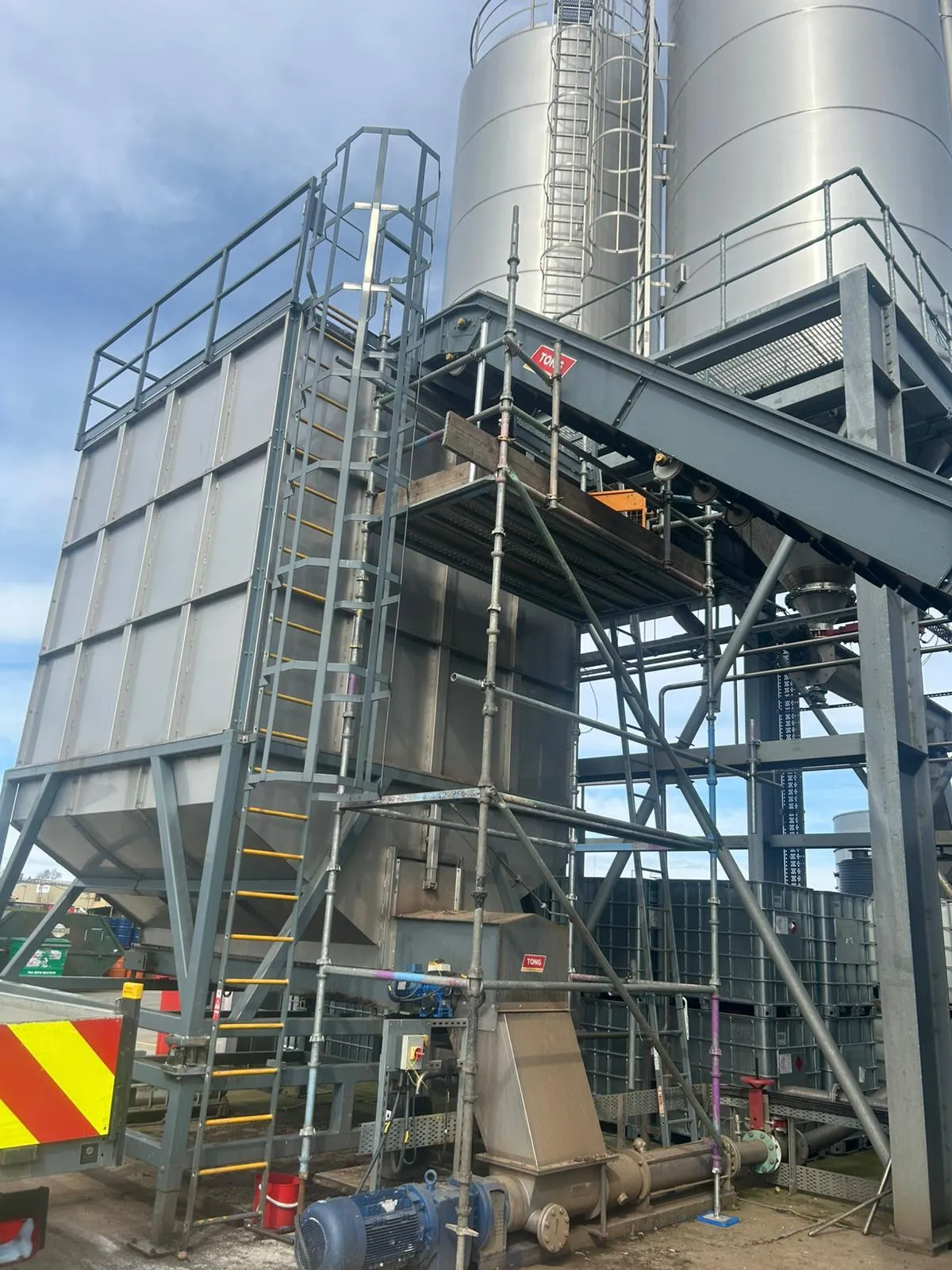Scaffold tower built around a hopper and conveyor beneath steel silos