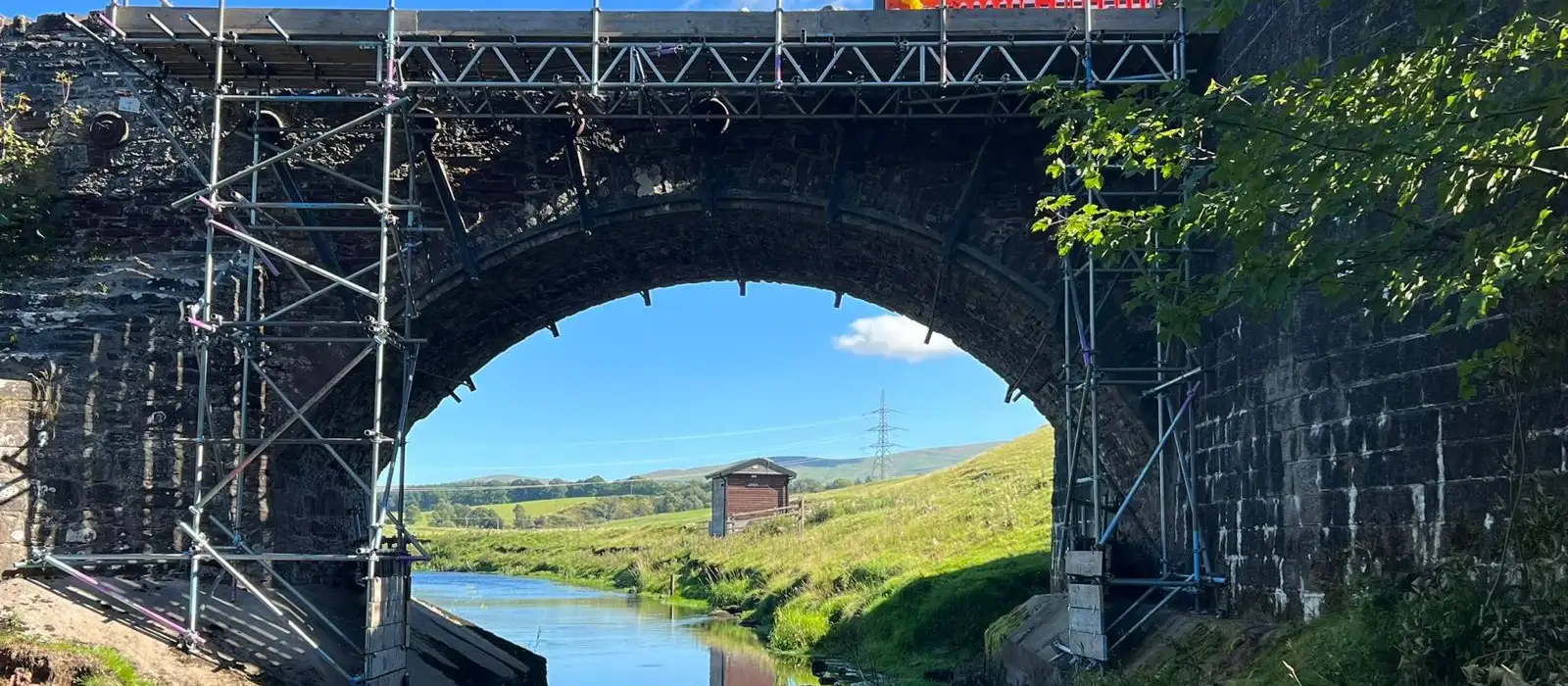 Scaffold with a beamed working platform across a stone arch bridge over a river